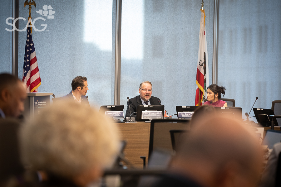 Business meeting with three people at a conference table, flags in background.