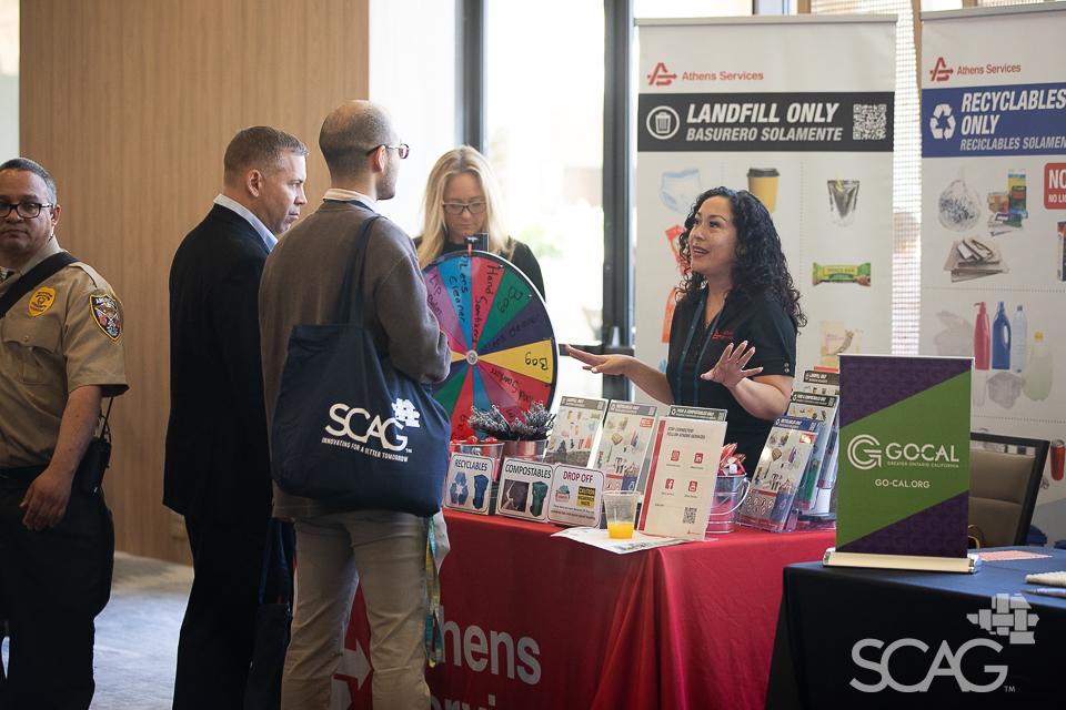 A group talks at an event booth with pamphlets and a multicolored wheel.